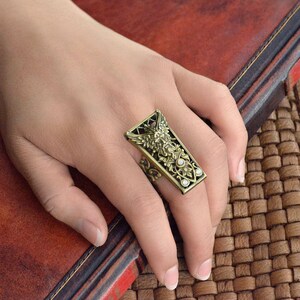 May include: A gold-toned ring with an intricate design featuring a bird and floral motifs. The ring has clear stones set in the design.