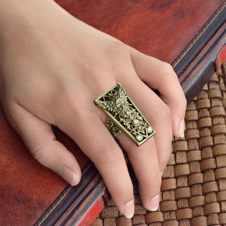 May include: A gold-toned ring with an intricate design featuring a bird and floral motifs. The ring has clear stones set in the design.