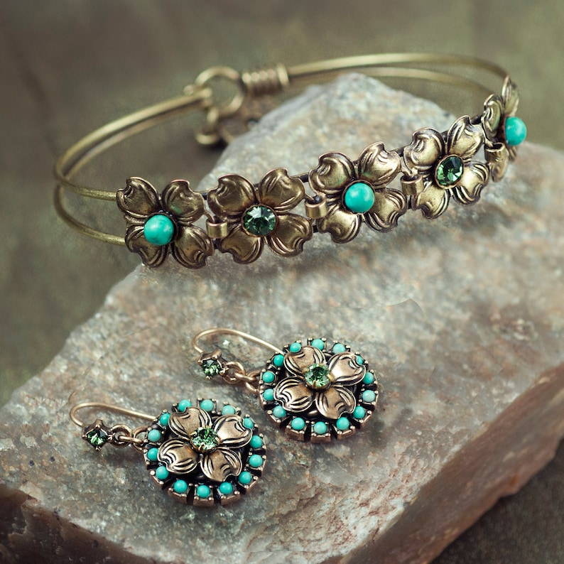 May include: A set of gold-tone jewelry with turquoise and green gemstones. The set includes a bangle bracelet and a pair of earrings, both featuring a floral design.