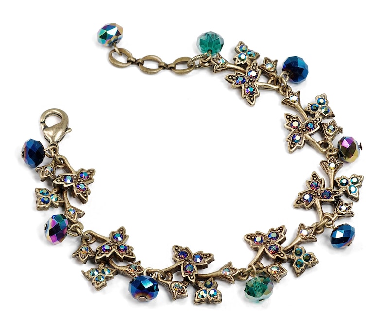 May include: A gold-tone bracelet with a vine design featuring iridescent blue and green crystals. The bracelet has a lobster claw clasp.