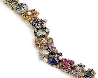 May include: A gold-tone bracelet with a series of charms, each featuring a different design. The charms are adorned with colorful enamel, rhinestones, and pearls. The bracelet is a statement piece with a whimsical and eclectic style.