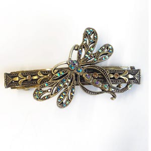 May include: A gold-toned butterfly hair clip with iridescent rhinestones. The butterfly is detailed with intricate filigree and has a long, thin bar clip.