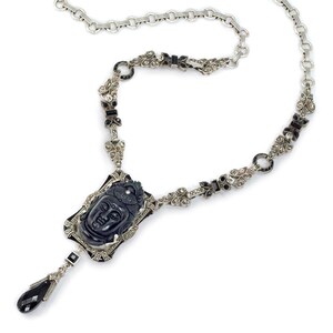May include: A silver necklace with a black onyx pendant featuring a carved Buddha face. The necklace is adorned with black and white marcasite stones.