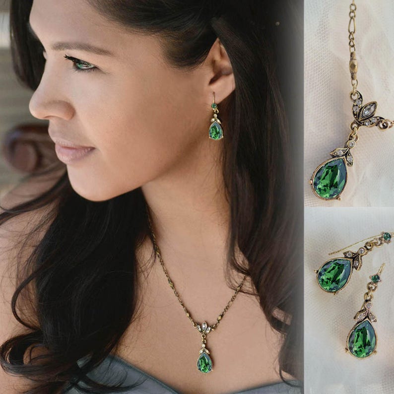 May include: A green teardrop-shaped pendant necklace and matching earrings with gold-tone metal accents. The necklace has a delicate chain and a small floral design above the pendant. The earrings are dangle style with a similar floral design.