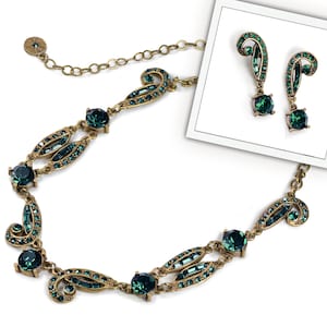 May include: A gold necklace and matching earrings with emerald green crystal accents. The necklace features a delicate chain and a repeating pattern of swirls and leaves. The earrings are drop style with a single emerald green crystal at the bottom.