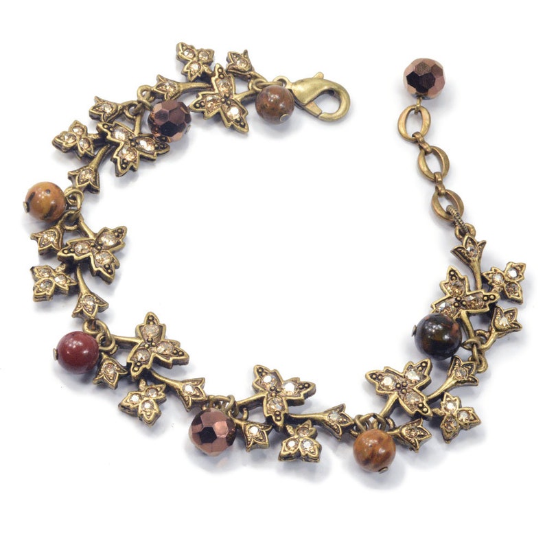 May include: A gold-tone bracelet with a leafy design and brown, red, and clear beads.