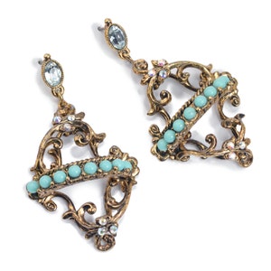 May include: A pair of gold-tone earrings with a delicate filigree design. The earrings feature a row of turquoise beads and clear rhinestones.