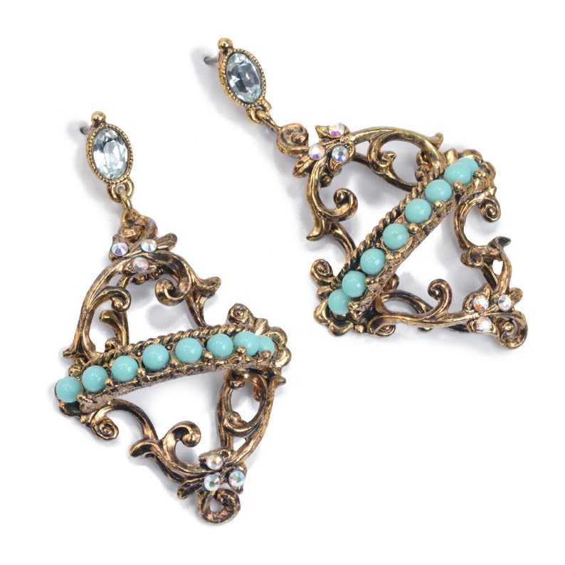 May include: A pair of gold-tone earrings with a delicate filigree design. The earrings feature a row of turquoise beads and clear rhinestones.