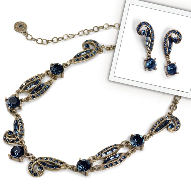 May include: A gold necklace and earrings set with a blue crystal design. The necklace features a delicate chain with a pendant that has a swirling pattern and blue crystals. The earrings are drop earrings with a similar swirling pattern and blue crystals.