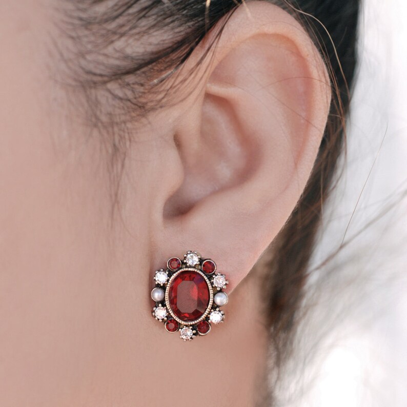 Puede incluir: Un par de pendientes de piedras preciosas rojas y blancas con un dise&ntilde;o floral. Los pendientes presentan una piedra roja grande rodeada de piedras blancas m&aacute;s peque&ntilde;as.