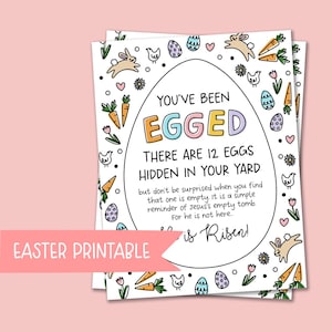 May include: Two white Easter printable cards with an egg-shaped design. The cards feature the text "YOU'VE BEEN EGGED" and "THERE ARE 12 EGGS HIDDEN IN YOUR YARD". The cards are decorated with bunnies, carrots, eggs, and flowers. The text "Easter Printable" is also included.