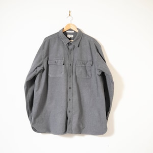 Może przedstawiać: Szara koszula z długim rękawem zapinana na guziki, z dwoma kieszeniami na piersi.