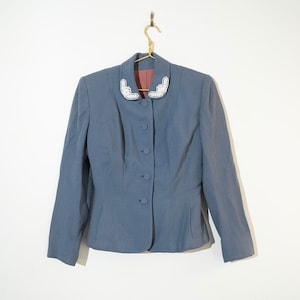 May include: A blue blazer with a white beaded collar. The blazer has a button-up front and long sleeves.