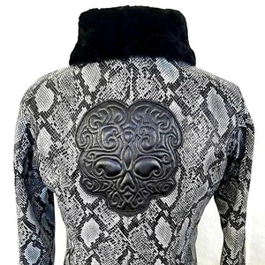 Puede incluir: Chaqueta con estampado de piel de serpiente en blanco y negro, con cuello de piel sintética negra. La espalda presenta una gran aplicación de calavera de cuero negro con detalles intrincados. La chaqueta tiene puños y dobladillo de canalé.