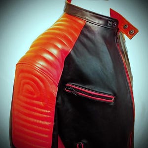 May include: A black and red leather jacket with a quilted shoulder design. The jacket features a red zipper and accents, with a classic collar and a tailored fit. The jacket is displayed on a mannequin, showcasing its sleek and modern design.