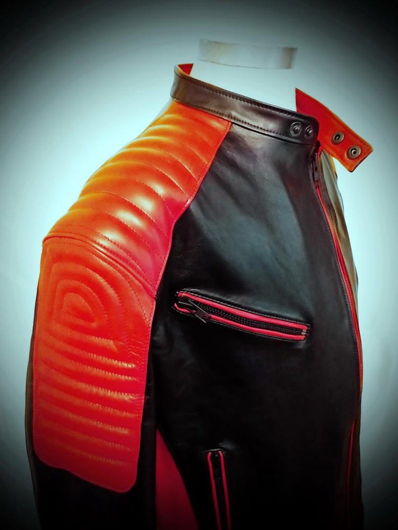 May include: A black and red leather jacket with a quilted shoulder design. The jacket features a red zipper and accents, with a classic collar and a tailored fit. The jacket is displayed on a mannequin, showcasing its sleek and modern design.