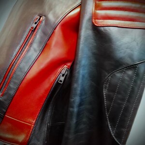 May include: A close-up of a leather jacket with a mix of black, brown, and red panels. The jacket features a zippered front, a quilted shoulder detail, and a sleek, modern design. The leather appears to be high-quality.