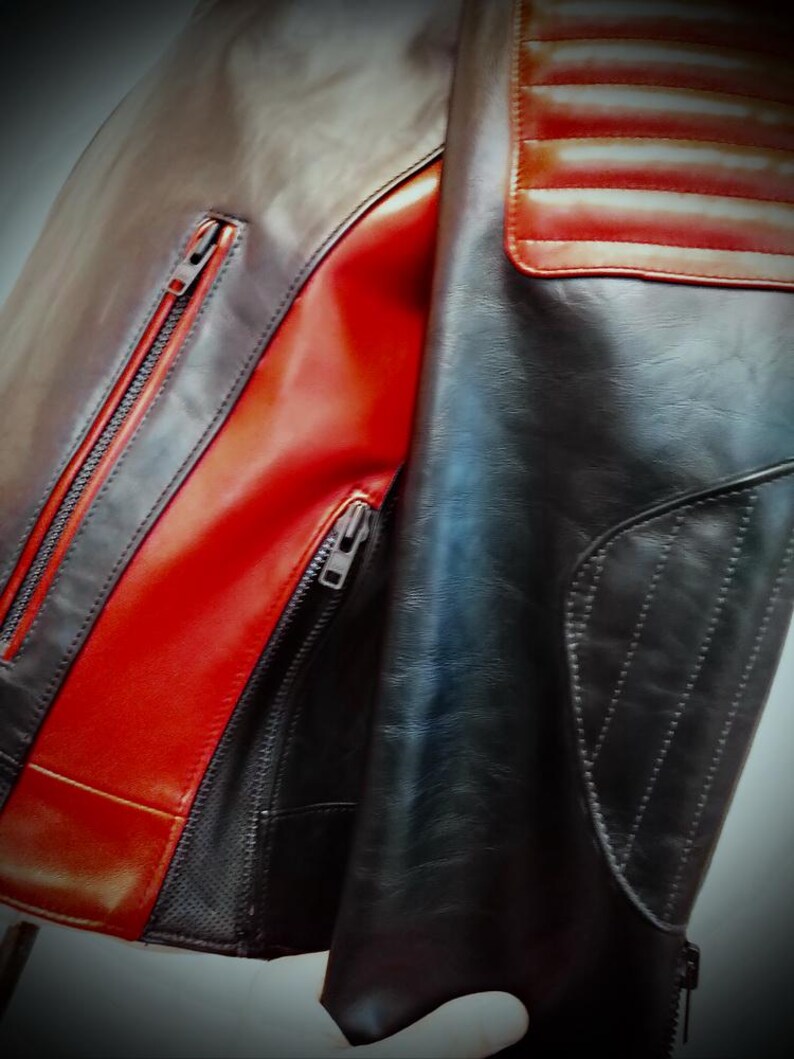 May include: A close-up of a leather jacket with a mix of black, brown, and red panels. The jacket features a zippered front, a quilted shoulder detail, and a sleek, modern design. The leather appears to be high-quality.