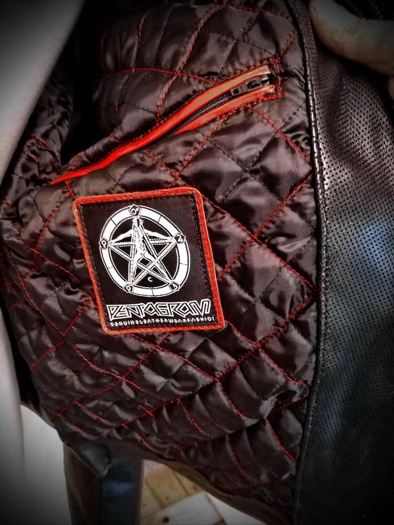 May include: Close-up of the interior of a black leather jacket. The quilted lining is dark brown with red stitching. A rectangular patch with a white pentagram design and the word "PENTAGRAM" is sewn on the lining. A red zipper is visible.