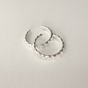 A pair of sterling silver ear cuffs are overlapping on a white surface.