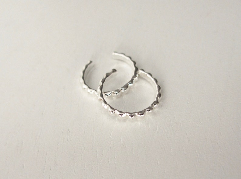 A pair of sterling silver ear cuffs are overlapping on a white surface.