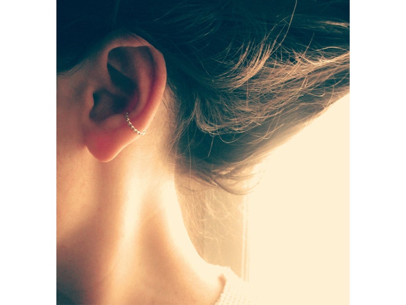 A woman with her head turned displays a sterling silver ear cuff for unpierced ears. It sits at the bottom of the outer cartilage, in the low conch position.