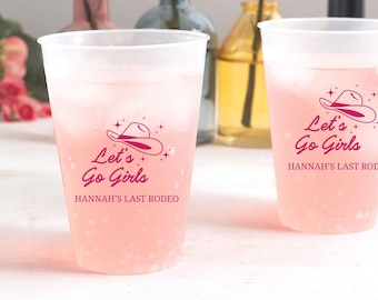 May include: Two translucent plastic cups filled with a light pink beverage and ice. Each cup features a pink graphic of a cowboy hat, the text "Let's Go Girls," and the personalized text "HANNAH'S LAST RODEO" printed in a matching pink font.