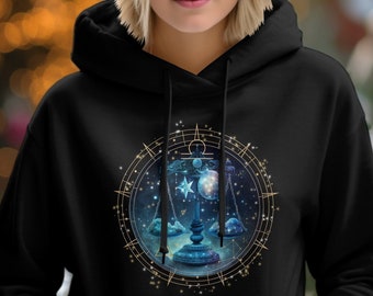 May include: Black hoodie featuring a celestial Libra design. The graphic includes a scale, stars, and a moon, all within a circular frame. The artwork is in shades of blue, gold, and white.