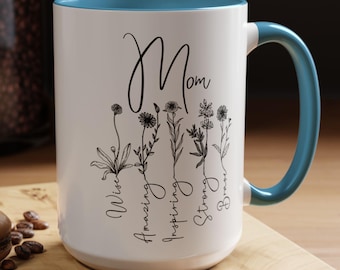 May include: A white ceramic mug with a blue interior and handle, featuring black line art of five wildflowers. Each flower is paired with a descriptive word: Wise, Amazing, Inspiring, Strong, and Brave. The word Mom is written in script above.