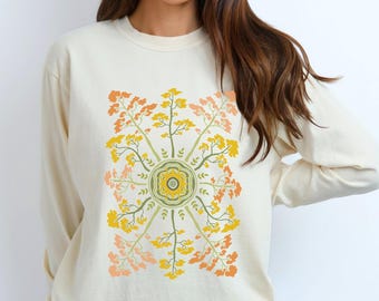 May include: Cream-colored long-sleeve sweatshirt featuring a colorful floral design. The design includes yellow, orange, and green branches arranged in a circular pattern. The sweatshirt is made of a soft material.