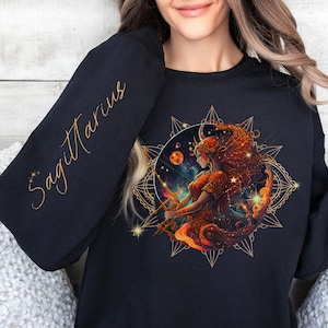 May include: Black sweatshirt with a gold Sagittarius zodiac sign design. The design features a woman with a bow and arrow, surrounded by stars and a mandala.