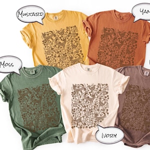 May include: Five different colored t-shirts: mustard, yam, moss, ivory, and espresso. Each shirt features a brown graphic of animals and floral elements. The shirts are short-sleeved and have a relaxed fit.