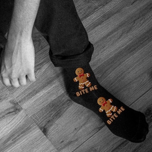 Puede incluir: Un par de calcetines negros con un diseño de hombre de jengibre y el texto "Bite Me" en cada calcetín.