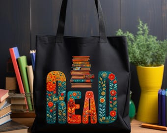 May include: Black tote bag with the word "READ" in colorful floral letters. A stack of books is between the "E" and "A". The bag has two black handles and is made of a sturdy material. The background includes books and a plant.