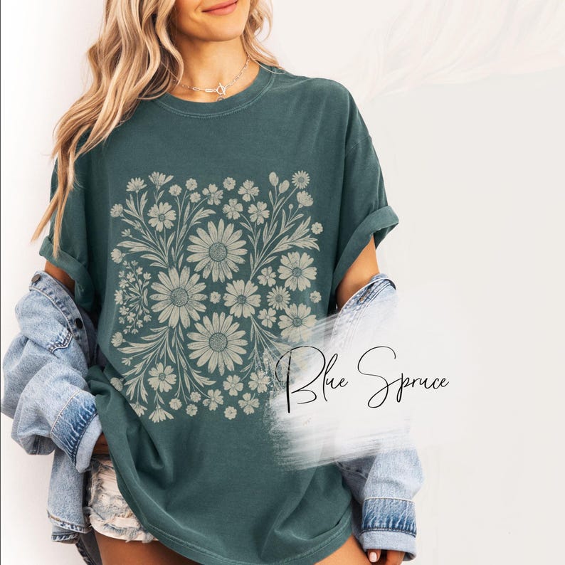 Pode incluir: Camiseta verde-azulado com um design floral com margaridas e outras flores em um padr&atilde;o quadrado. O texto "Blue Spruce" est&aacute; escrito em it&aacute;lico no canto inferior direito.