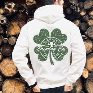 May include: White hoodie with a green shamrock design on the back. The shamrock features the text "St. Patrick's Brewing Co. Since 1982, Premium Lucky Spirits". The hoodie has a hood and a front pocket.
