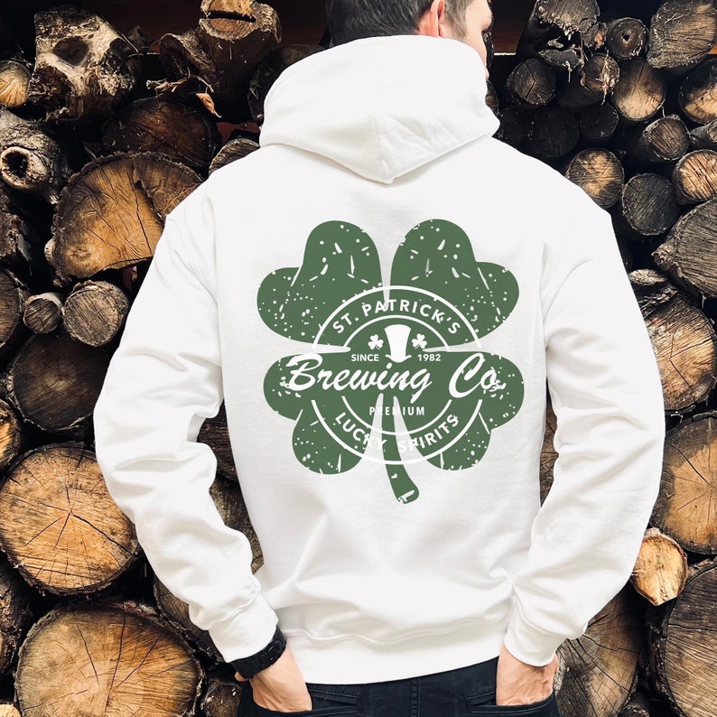 May include: White hoodie with a green shamrock design on the back. The shamrock features the text "St. Patrick's Brewing Co. Since 1982, Premium Lucky Spirits". The hoodie has a hood and a front pocket.