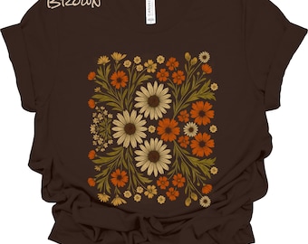 May include: A dark brown short-sleeve t-shirt featuring a central graphic print of various flowers in shades of cream, orange, and olive green. The word BROWN is printed in the upper left corner, and a white brand label is visible at the neck.