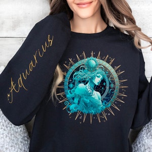 Puede incluir: Sudadera negra con una ilustraci&oacute;n dorada y azul del signo astrol&oacute;gico Acuario. La palabra "Aquarius" est&aacute; escrita en letras doradas en la manga.
