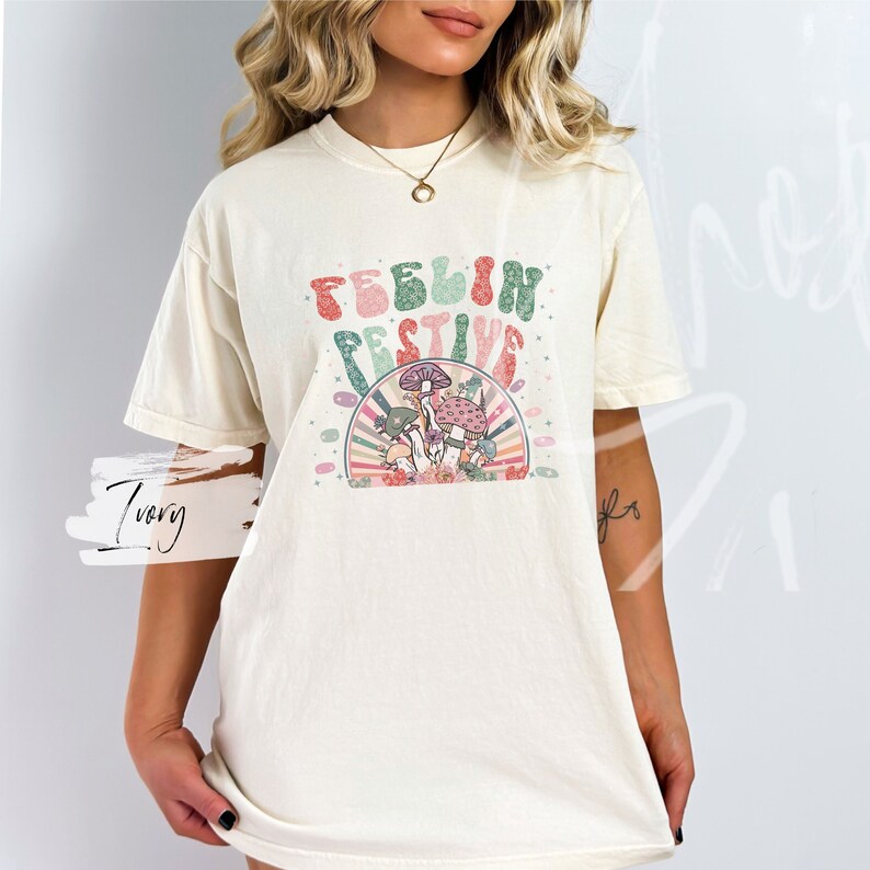 Peut inclure: Un t-shirt cr&egrave;me avec un motif r&eacute;tro de champignons et le texte "Feelin Festive".