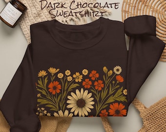 May include: A dark chocolate brown long-sleeve sweatshirt featuring a graphic print of various wildflowers in shades of orange, yellow, and cream with green stems and leaves. The text "DARK CHOCOLATE SWEATSHIRT" is printed above the garment.