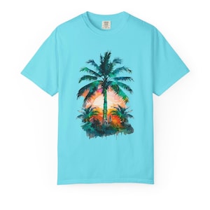 May include: A light blue t-shirt featuring a watercolor design of a tropical sunset with palm trees. The artwork showcases a vibrant sunset with shades of orange, pink, and yellow, creating a scenic beach theme.