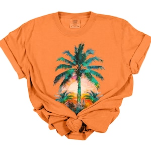 May include: Orange t-shirt featuring a tropical sunset scene with a large palm tree in the center. The palm tree has green and blue leaves, with a colorful sunset in the background. The shirt is knotted at the bottom.