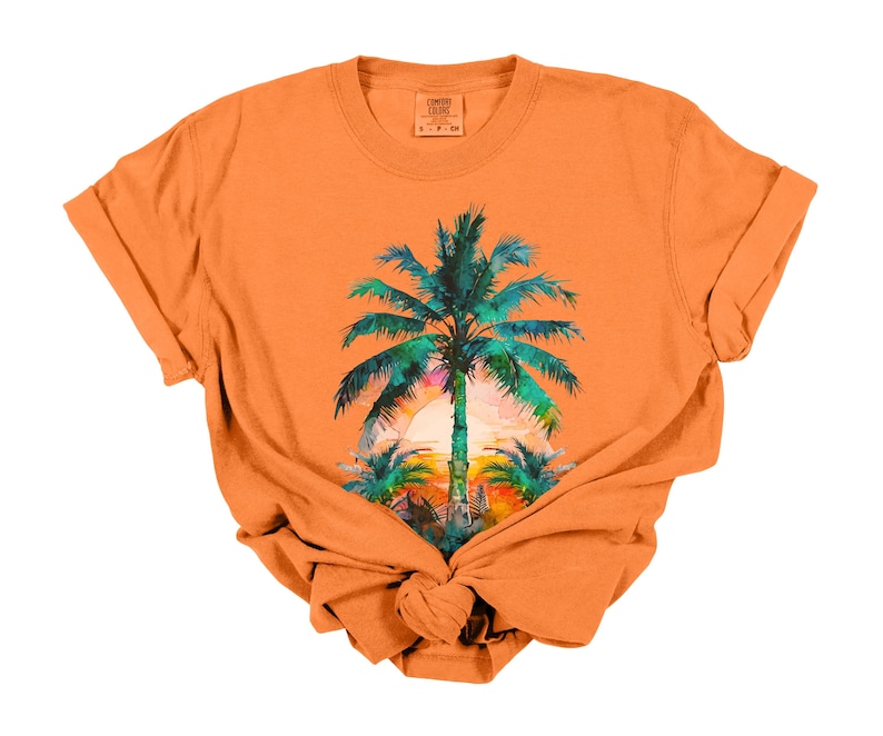 May include: Orange t-shirt featuring a tropical sunset scene with a large palm tree in the center. The palm tree has green and blue leaves, with a colorful sunset in the background. The shirt is knotted at the bottom.
