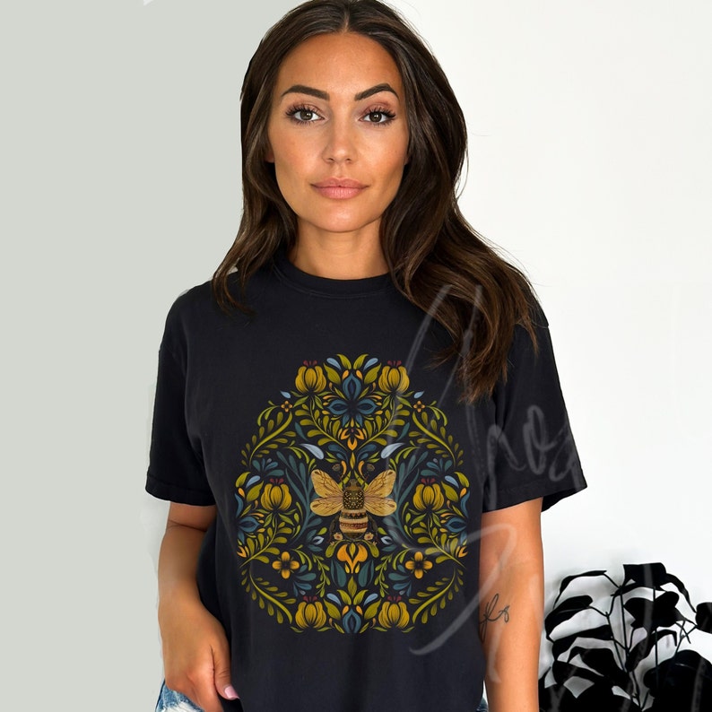 May include: Black t-shirt with a floral design featuring a bee in the center. The design is in shades of yellow, green, blue, and brown.
