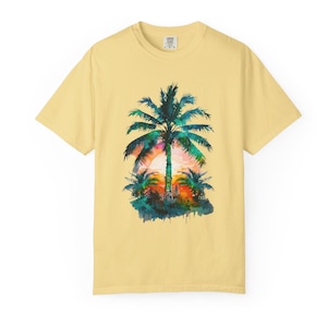 May include: A light yellow t-shirt featuring a watercolor design of a palm tree at sunset. The palm tree is green with a colorful sunset in the background. The shirt is a short-sleeved crew neck.