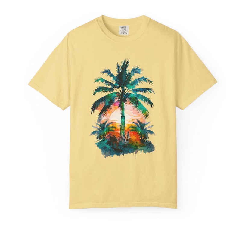 May include: A light yellow t-shirt featuring a watercolor design of a palm tree at sunset. The palm tree is green with a colorful sunset in the background. The shirt is a short-sleeved crew neck.