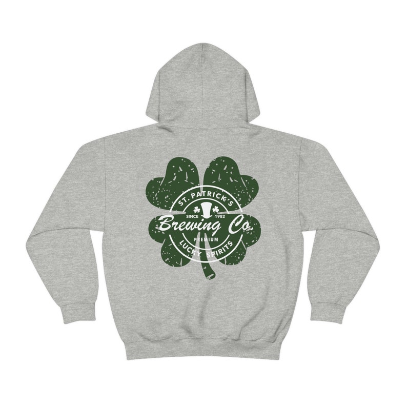 May include: A heather gray hoodie with a green shamrock design. The shamrock features the text "St. Patrick's Brewing Co. Since 1982" and "Premium Lucky Spirits". The hoodie has a drawstring hood and a kangaroo pocket.