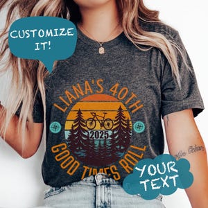 May include: Dark grey t-shirt with a circular design featuring a bicycle, trees, and a sunset. Text includes "LIANA'S 40TH GOOD TIMES ROLL 2025" and "CUSTOMIZE IT!" and "YOUR TEXT" in speech bubbles.