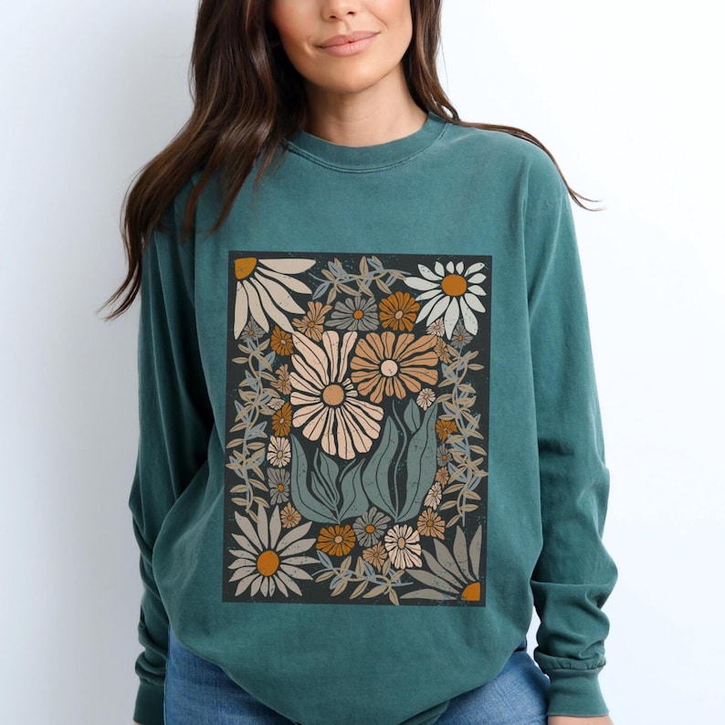 May include: Teal-colored long-sleeve sweatshirt featuring a floral design. The graphic includes various flowers in shades of cream, orange, and green, set against a dark background. The sweatshirt has a crew neck and a relaxed fit.
